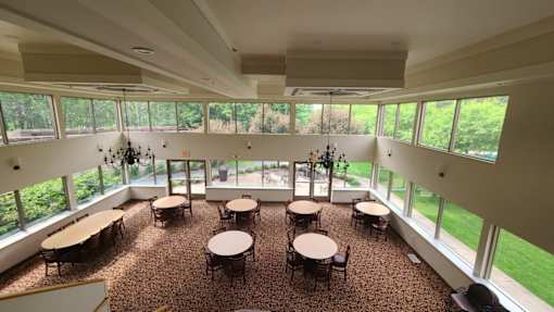 A large room with tables and chairs and windows overlooking a green lawn.