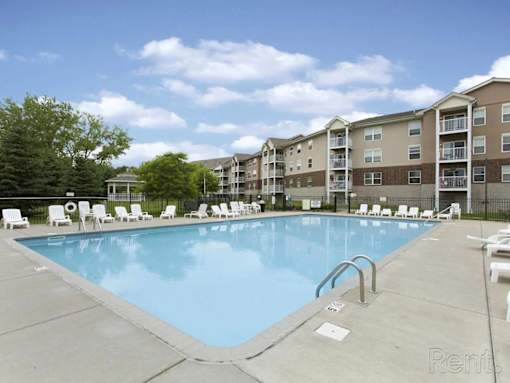A large swimming pool surrounded by lounge chairs and apartment buildings.