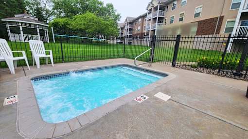 A small pool surrounded by a black fence and a white chair.