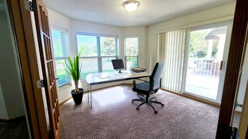 A room with a desk, chair, and potted plant.
