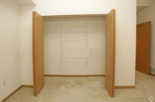 A room with a white wall and a wooden wardrobe with hanging rods.