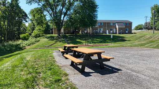 A picnic table sits on a gravel area in front of a grassy field and a building.