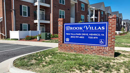 A brick sign that says Brook Villas in front of some houses.