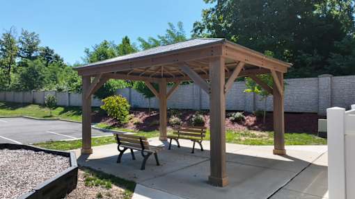 A wooden pavilion with two benches sits in a parking lot.