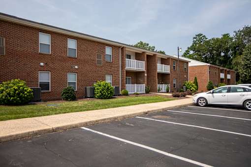 A white car is parked in a parking lot in front of a brick apartment building.