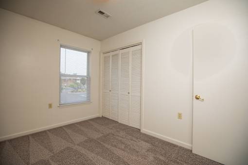 A room with a carpeted floor, a window with blinds, a closed door, and a ceiling fan.