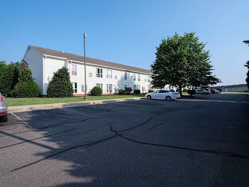 A white car is parked in front of a white building with a brown roof.