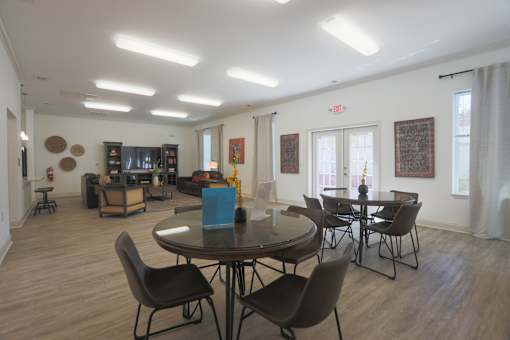 A room with a round table and chairs in the foreground and a living room in the background.