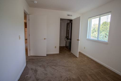 A room with a brown carpet and a window with blinds.