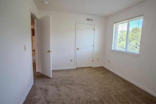 A room with a carpeted floor, a white door, and a window with blinds.