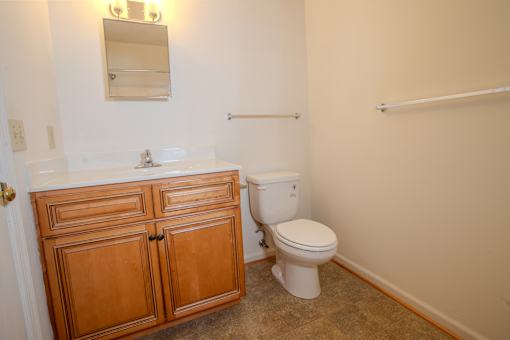 A white toilet sits in a bathroom with a wooden cabinet and a mirror above it.