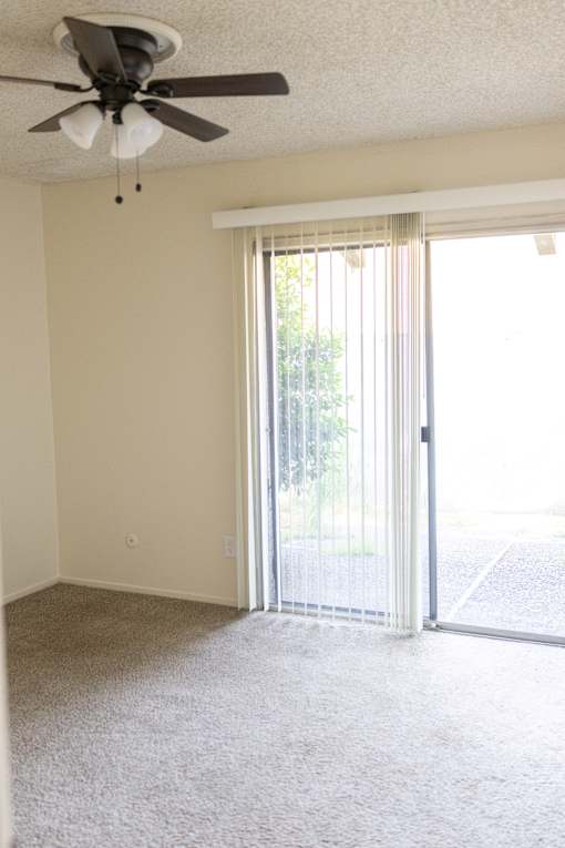 A room with a ceiling fan and sliding glass doors.