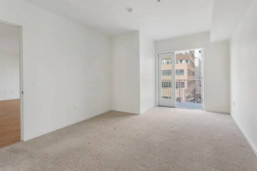 A large empty room with a carpeted floor and a window showing a building outside.