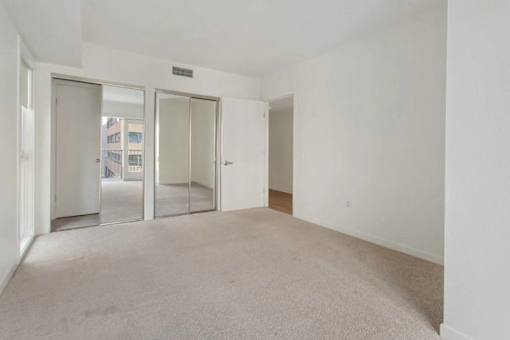 A room with white walls and carpeted floor with a door on the left and a door on the right.