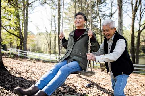 An elderly woman is being swung by a man in a park.