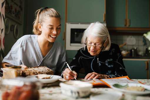 A woman and an elderly woman are sitting at a table with plates of food in front of them.