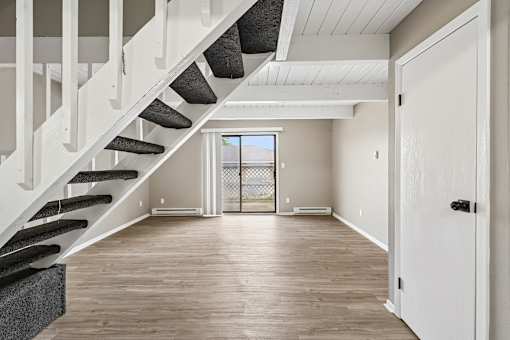 A white staircase with black steps leads to a bright room with a sliding glass door.