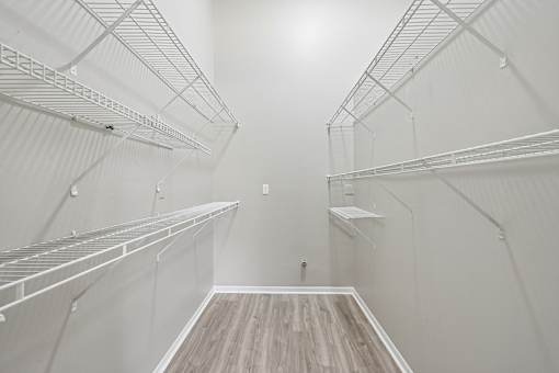 Empty walk-in closet with white shelves and wood flooring.