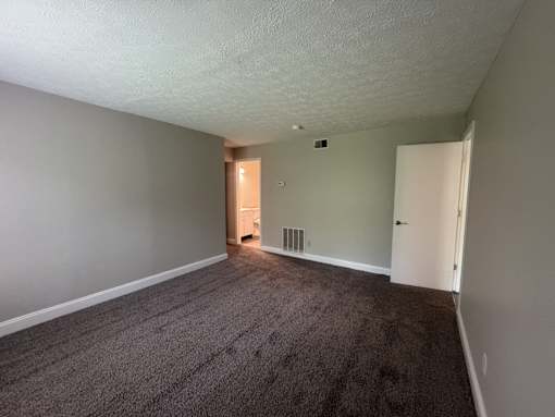A room with a carpeted floor and a heater vent on the wall.