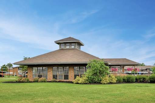 A building with a brown roof and a tower on top is surrounded by greenery.