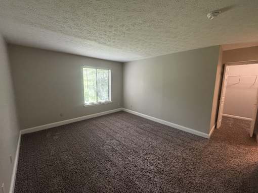 A room with a carpeted floor and a window with blinds.
