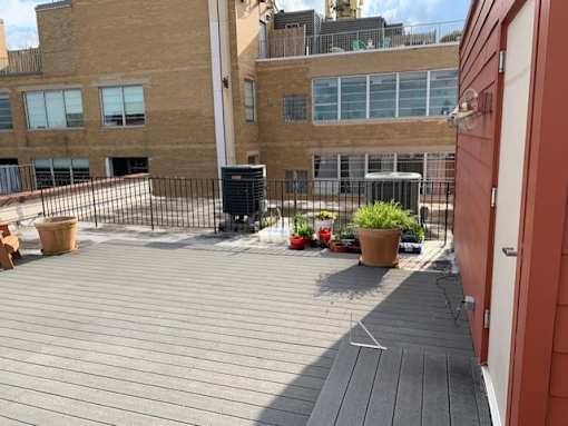 A wooden deck with a black trash can and a red door.