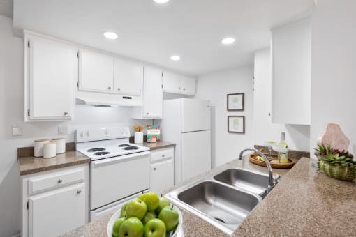 a kitchen with white appliances and white cabinets and a sink with apples on the counter