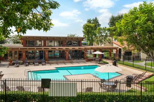 a swimming pool and patio with chairs and umbrellas in front of a house