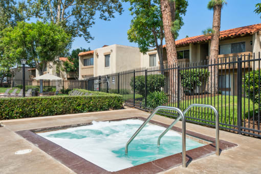 a hot tub in a fenced in area with trees and a house