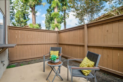 a patio with two chairs and a table in front of a fence