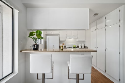 a kitchen with white cabinets and a counter with two white chairs