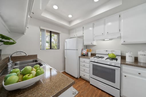 a kitchen with white cabinets and a sink with a bowl of fruit on the counter