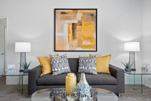 a living room with a gray couch with yellow pillows and a glass coffee table