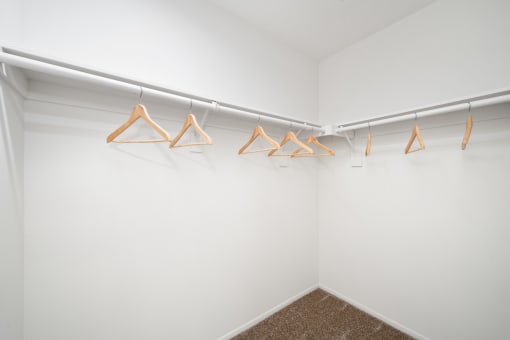 a walk in closet with white walls and wooden clothes hangers