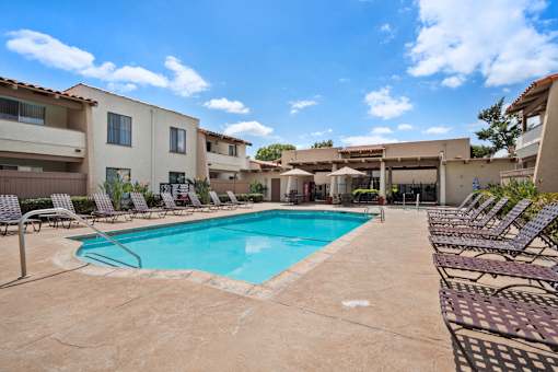 A swimming pool surrounded by lounge chairs in front of apartment buildings.