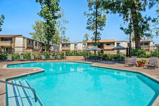A swimming pool surrounded by trees and chairs.