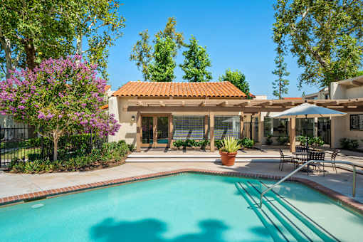 A pool in a backyard with a patio and a building in the background.