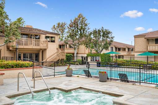 A pool with a hot tub in the middle of a patio surrounded by chairs and trees.
