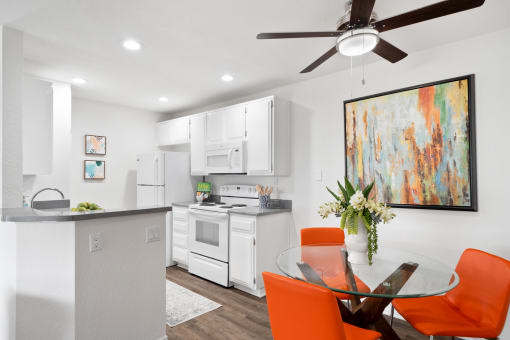 a white kitchen and dining room with orange chairs and a table