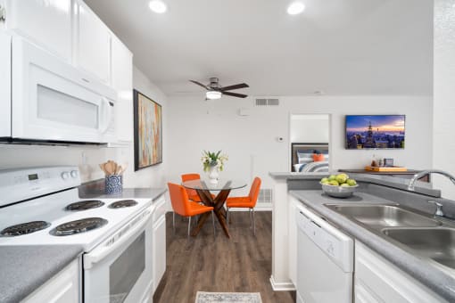a kitchen with white appliances and a dining room with orange chairs