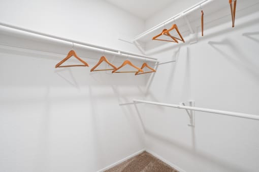 a walk in closet with white walls and orange hooks