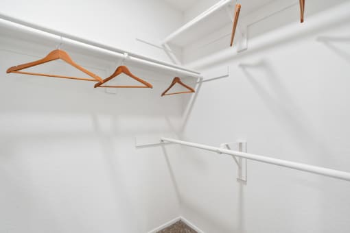 a walk in closet with white walls and white rods with hangers