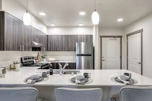 A modern kitchen with a white countertop and grey chairs.