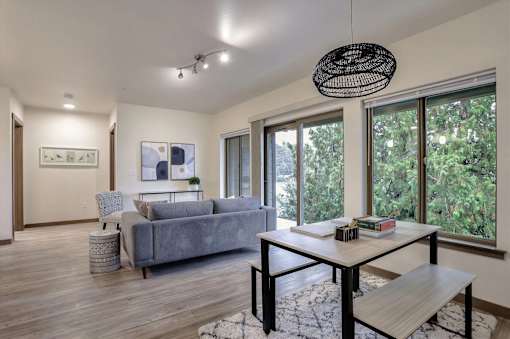 A living room with a grey couch, a white table, and a large window.