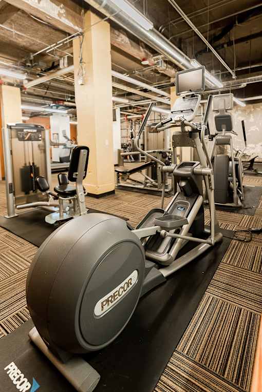 A Precor elliptical trainer is on a black mat in a gym.