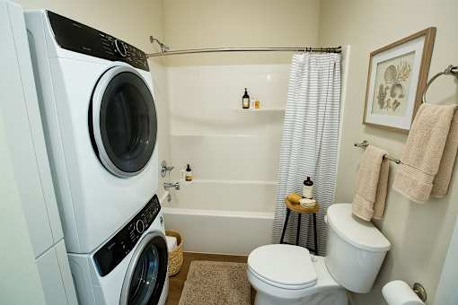 A white washing machine is in a bathroom with a toilet and a shower.