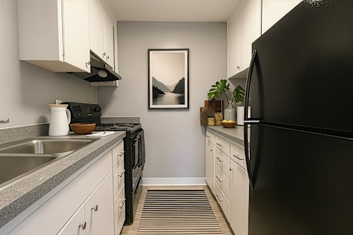 A black refrigerator is on the right in a kitchen with white cabinets.