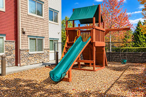 A wooden playset with a green slide in front of a red house.