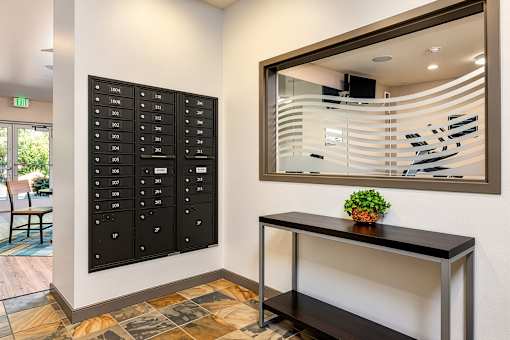 A black mailbox with white numbers is on the wall next to a desk with a potted plant on it.