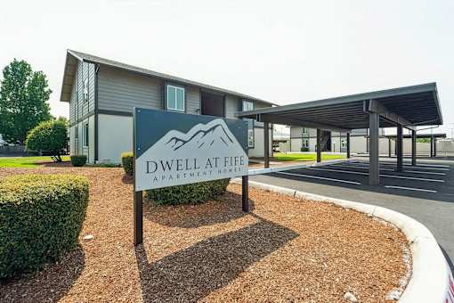 A sign for Dwell at Life Apartment Homes stands in front of a modern building.
